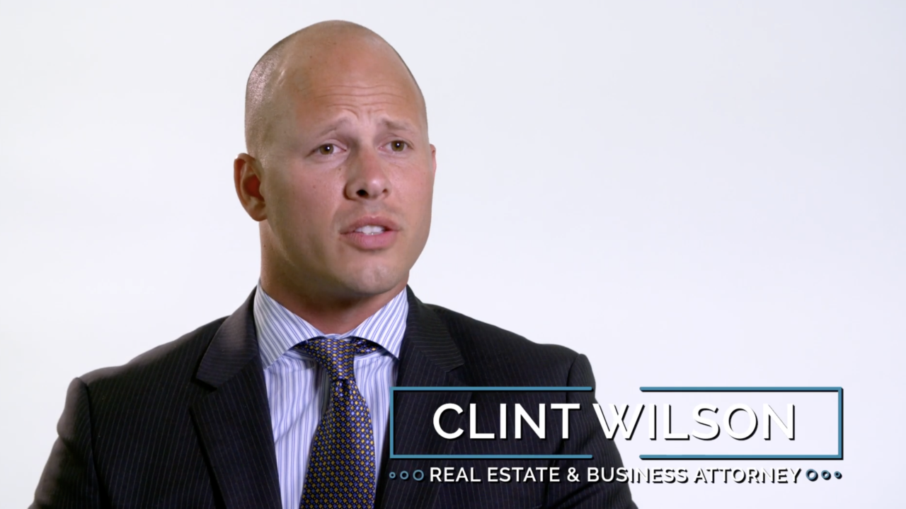 A man in a suit and tie speaks in front of a plain white background. Text on the image reads Clint Wilson, Real Estate & Business Attorney.