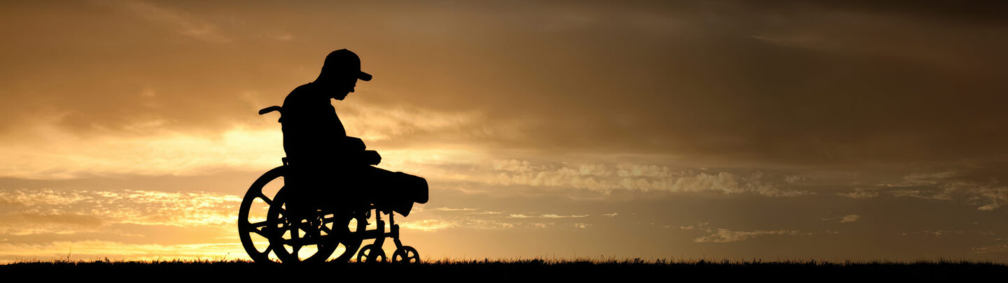 Silhouette of a person sitting in a wheelchair outdoors at sunset, with a dramatic sky and clouds in the background.
