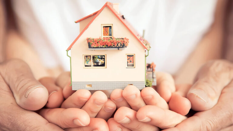 Two pairs of hands, one adult and one child, gently holding a small model house together, symbolizing family, protection, and homeownership.