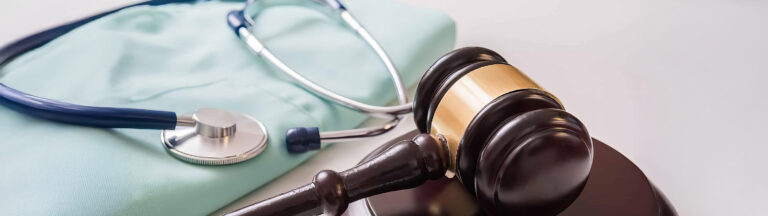 A judges gavel rests beside a stethoscope and light blue scrubs, symbolizing the intersection of healthcare and law.
