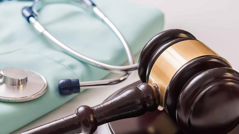 A judges gavel rests beside a stethoscope and light blue scrubs, symbolizing the intersection of healthcare and law.