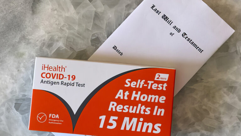 A COVID-19 at-home rapid test kit and a white envelope labeled Test, Billing and Treatment are placed on a gray marble surface.