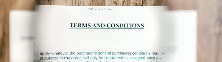 A close-up of an open document showing the heading TERMS AND CONDITIONS in bold, with blurred text and a wooden surface in the background.
