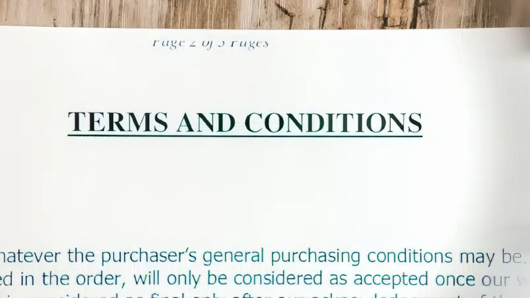 A close-up of an open document showing the heading TERMS AND CONDITIONS in bold, with blurred text and a wooden surface in the background.