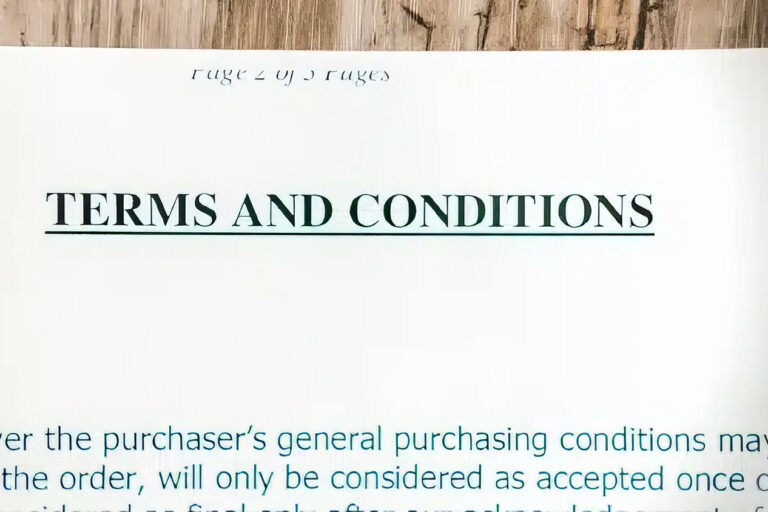 A close-up of an open document showing the heading TERMS AND CONDITIONS in bold, with blurred text and a wooden surface in the background.