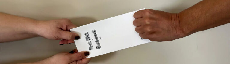 Two hands on the left pull on a legal document while a fist on the right tightly grabs the other end, suggesting a struggle or dispute over the paper. The background is a plain, light-colored wall.