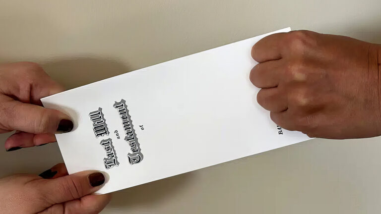 Two hands on the left pull on a legal document while a fist on the right tightly grabs the other end, suggesting a struggle or dispute over the paper. The background is a plain, light-colored wall.