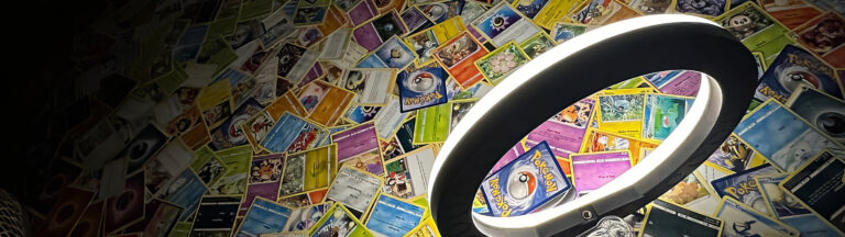 A ring light is positioned in front of a colorful wall covered with overlapping Pokémon trading cards, creating a vibrant and playful background.
