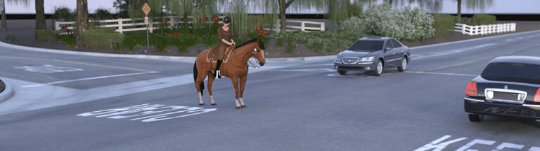 A person wearing a helmet rides a brown horse across an intersection while two cars approach from opposite directions. Trees, bushes, and a white fence are visible in the background.