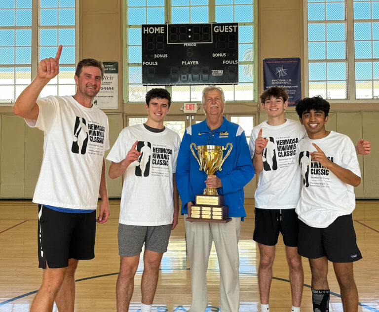 Five men stand smiling on a basketball court, four wearing matching Hermosa Kiwanis Classic shirts and holding up one finger, while the fifth man in a blue jacket holds a large trophy.
